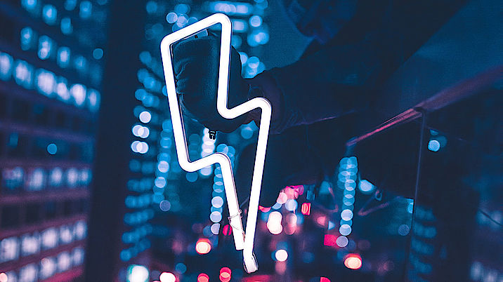 Ein Neonschild in Form eines Blitzes in der Dunkelheit in einer Großstadt (Quelle: Max Bender/unsplash.com)